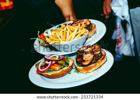 Two plates with burgers and french fries on their way to being served in a restaurant, in retro 90\'s aesthetics.