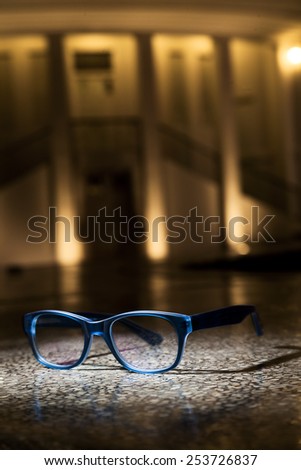 A pair of transparent blue rimmed glasses against a classical urban building background.