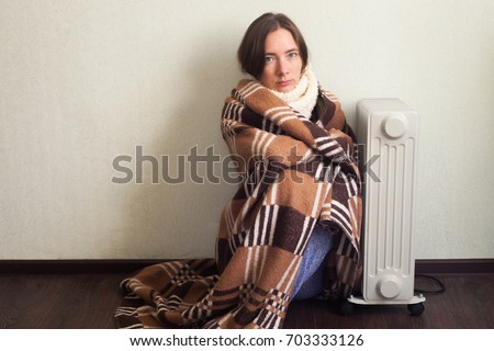 Young Cold Woman Wrapped In Blanket Sitting Near electric Heater At Home