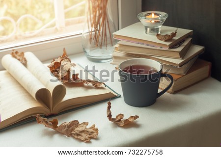 autumn still life. books, leaves, cup and dry tiny flowers in vase red candlestick on window. Concept of autumn reading time and romantic, Warm, cozy seat  opened book, rustic style home decor