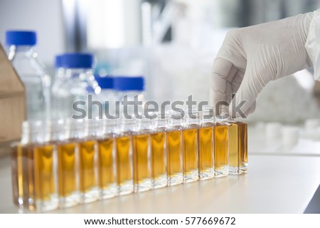 Lab / Laboratory closeup of hand in sterile gloves straighten out a glass bottle filled with liquid. E-Liquid, Chemical Filling, Manufacturing, Science, Scientist, Medicine, Chemistry, Pharmaceutical
