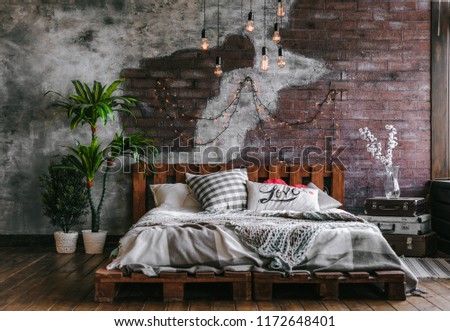 Stylish bedroom in loft style with lots of pillows and lots of light bulbs. Bed on brick wall background. Modern loft bedroom design.