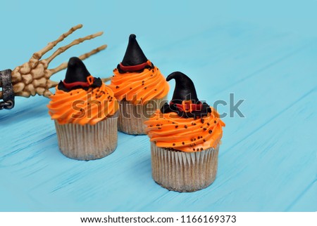 Halloween cupcakes. Witch hat cupcake. Halloween treats on wooden blue background with palm of the skeleton. Halloween background with copy space for text. Happy Halloween party. Monster party cupcake