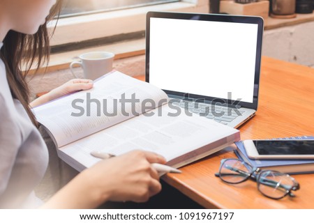 back view of young asian female student studying in the coffee shop with laptop at wooden table, a student opening a book for doing report or thesis in the cafe, education and working concept