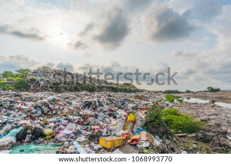 The large heap garbage dump extends parallel to the river,Garbage mountains with cloudy sky back ground in day light,Waste has petroleum products are the major.