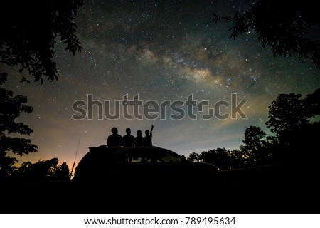 Silhouette of four friends watching milky way and pointing to the star on roof top of SUV car