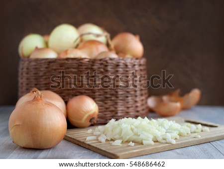 A lot of heads bulb onion in a wicker basket. Large onions in a large wicker bowl. Sliced onions on a cutting board to prepare meals. Bulb onion is good for health.