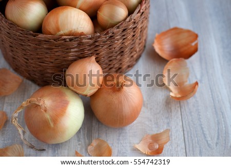 Large onion harvest in a wicker basket. Bulb onion is rich in vitamins, useful spring. Onion peel on a wooden background. Large onions can be seen from above.