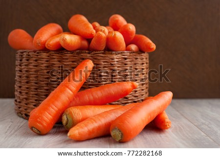 A lot of carrots in a wicker basket. Carrots in a wicker box and next to the box. Orange carrots washed. Carrots for diet and healthy eating. Vintage vegetables on a wooden background.