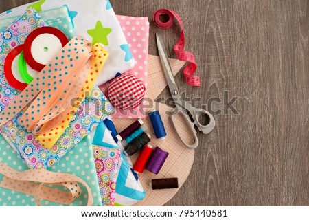 Sewing and objects for sewing. View from above. Fabric, tailoring scissors, centimeter tape, thread, ribbon, drawings are needed for sewing clothes. Sewing items are stacked together.