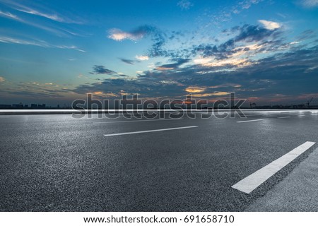 Asphalt road and the beautiful urban skyline at sunset