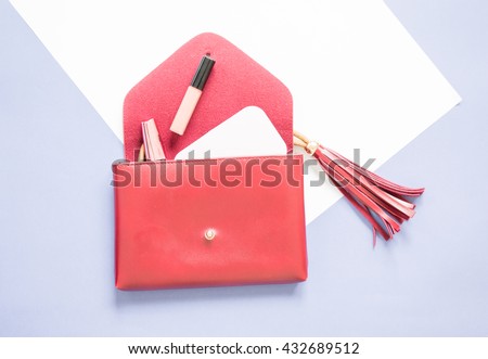 open red clutch bag design with tassel and cosmetics on white and blue background.
