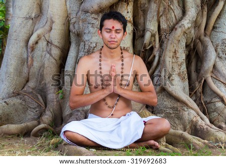 A young brahmin sits in meditation under a banyan tree in India