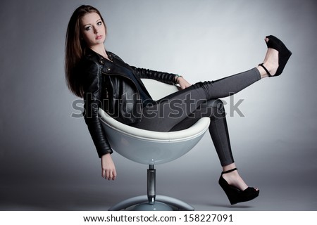 young woman posing on a stylish chair wearing leather jacket, pants and high pumps