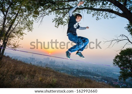 A man goes and shows tricks on the tightrope at the sunset and the city slack-line