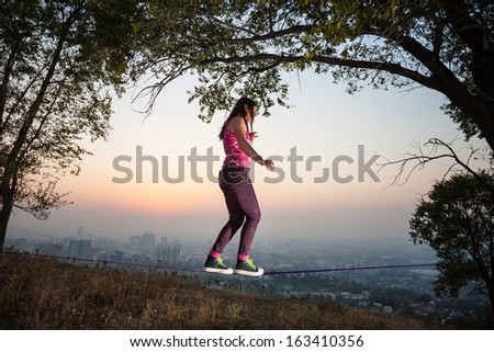 The girl goes and shows tricks on tightrope at sunset and the city slack-line