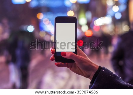 Young girl taking night view photos using mobile phone on the street
