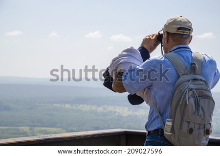 Elderly man looking binoculars pointing to the mountains