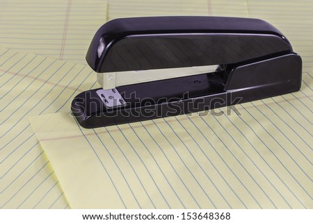 A black stapler sitting on top of yellow legal pad sheets.