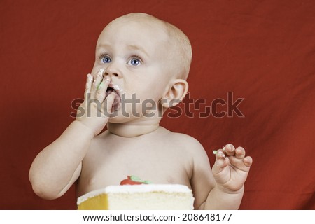 An infant boy eating birthday cake against a red background.