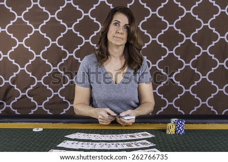 A woman sitting at a poker table playing cards with a brown background