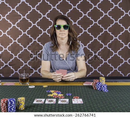 A woman sitting at a poker table wearing sunglasses playing cards with a brown background