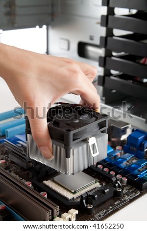 Assembling a high performance personal computer, Mounting Cooling Fan on CPU, opened PC case in background, shallow depth of field, focus on hand