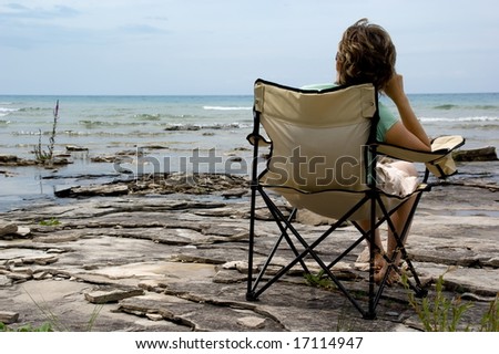 A woman resting on chair at the coastline. Huron lake, Canadian shield. Ontario, Canada.
