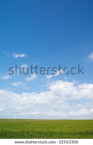 Simple summer background: green field and blue sky with clouds
