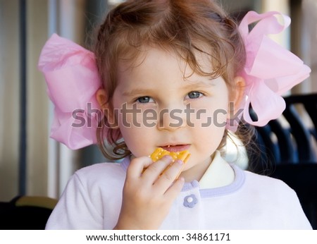 Cute little girl with big pink bows eating cookies