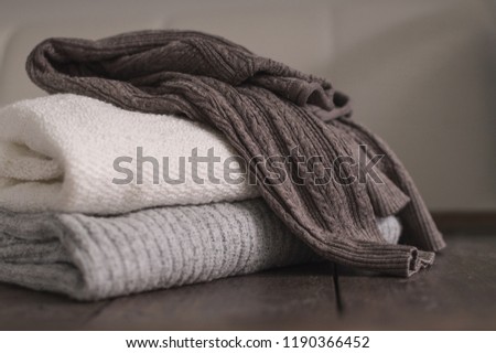 Stack of neatly folded woolen knitwear. Minimal lifestyle, capsule wardrobe. Autumn-winter men fashion wardrobe concept. Earth tones, horizontal copy space