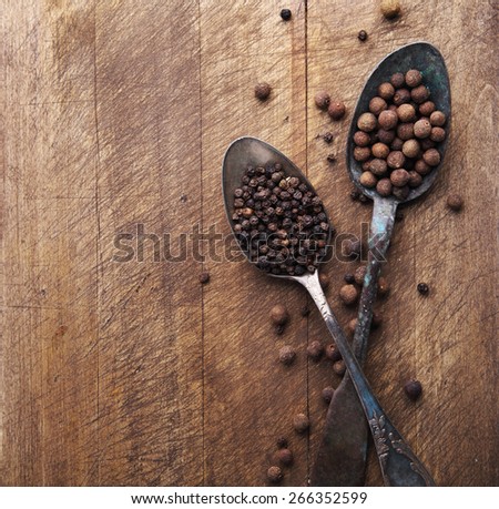 Image of two vintage spoons full of black peppercorn and allspice on rustic wooden cutting board