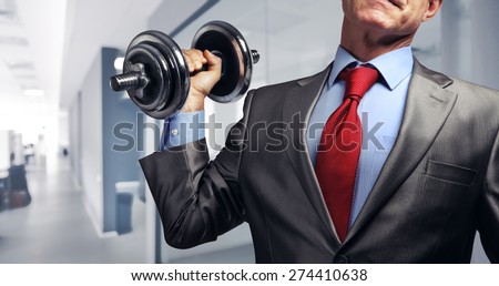 Image of businessman in suit raising dumbbell in office. Tax burden concept