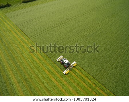 Aerial view of a tractor mowing a green fresh grass field, \
a farmer in a modern tractor mowing a green fresh grass field on a sunny day