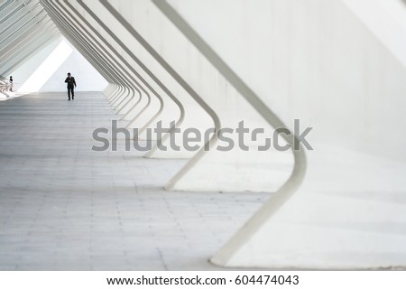 People in the architectural perspective. The sloping lines of the architecture. The man in the suit comes in a bright corridor in a modern building