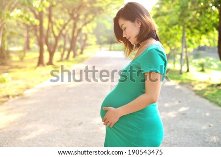 Beautiful pregnant Asian woman feeling lovely and Relax in the park with warm light in morning
