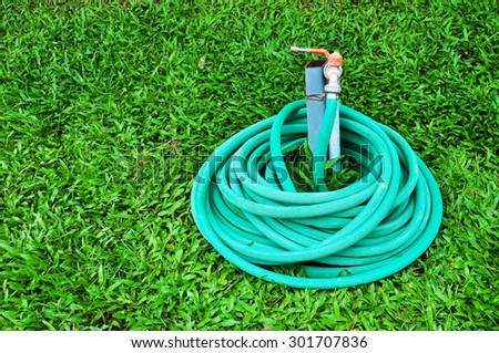 green garden hosepipe, green plastic sprayer hose for irrigation laying in garden on green grass, Garden hose coiled on green grass