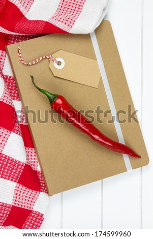 brown notebook with label tag, red checkered tea towel and chili pepper