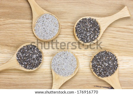 top-view of five spoons filled with black and white chia seeds on wooden surface