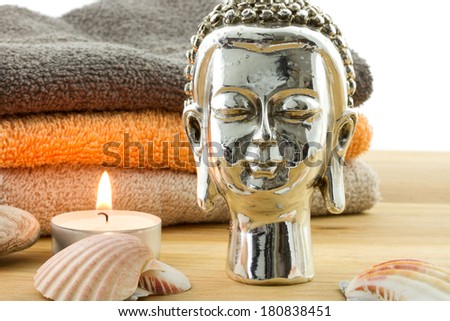 detail of buddha with candle, several shells and orange and brown towels on the background