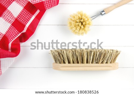 top-view of dish-washing brush and scrubbing brush and tea towel on white wooden surface