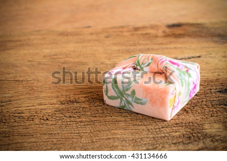 Gift box wrapped with Thai traditional style cloth tie on wood background, vignetted.