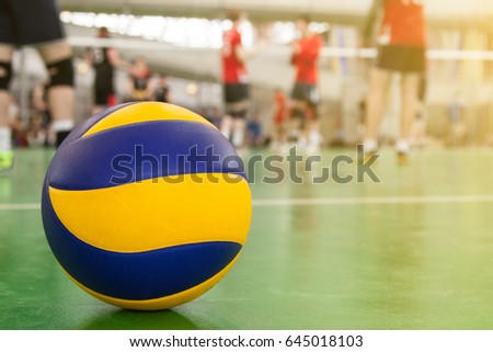 Yellow-blue volleyball on the floor in the gym, team of athletes playing volleyball