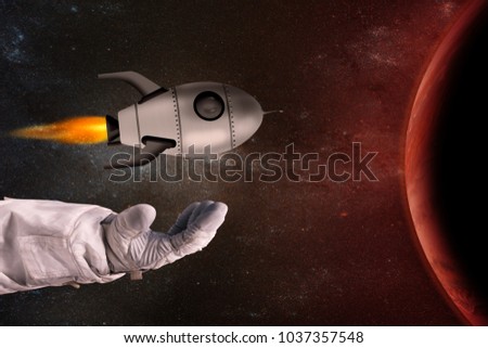 The toy rocket in the hands of the astronaut opposite the red planet. Elements of this image furnished by NASA.