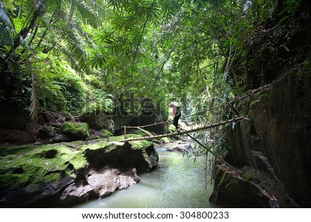 UBUD, BALI - CIRCA January 2011 - An unidentified woman crosses a bamboo bridge over a river in the forest. Hiking in Bali is a popular for tourists with many treks through rice paddies and forests.