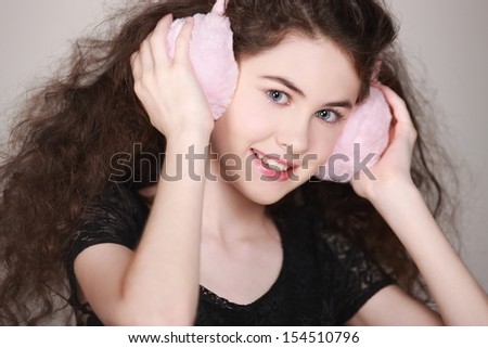 Beautiful girl with earmuffs. Portrait of a young woman with big hair, holding her earmuffs & smiling into camera.  Processed from RAW, detailed retouching.