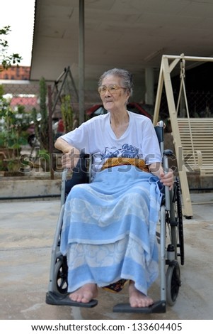 old lady at golden age sitting on wheel chair at house front yard
