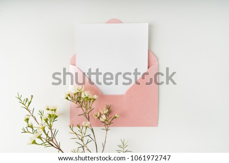 Minimal composition with a pink envelope, white blank card and a wax flower on a white background. Mockup with envelope and blank card. Flat lay. Top view.