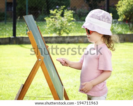 Little girl drawing on the board in the garden