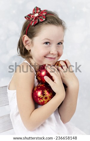 Happy little girl with freckles on her nose holding christmas balls